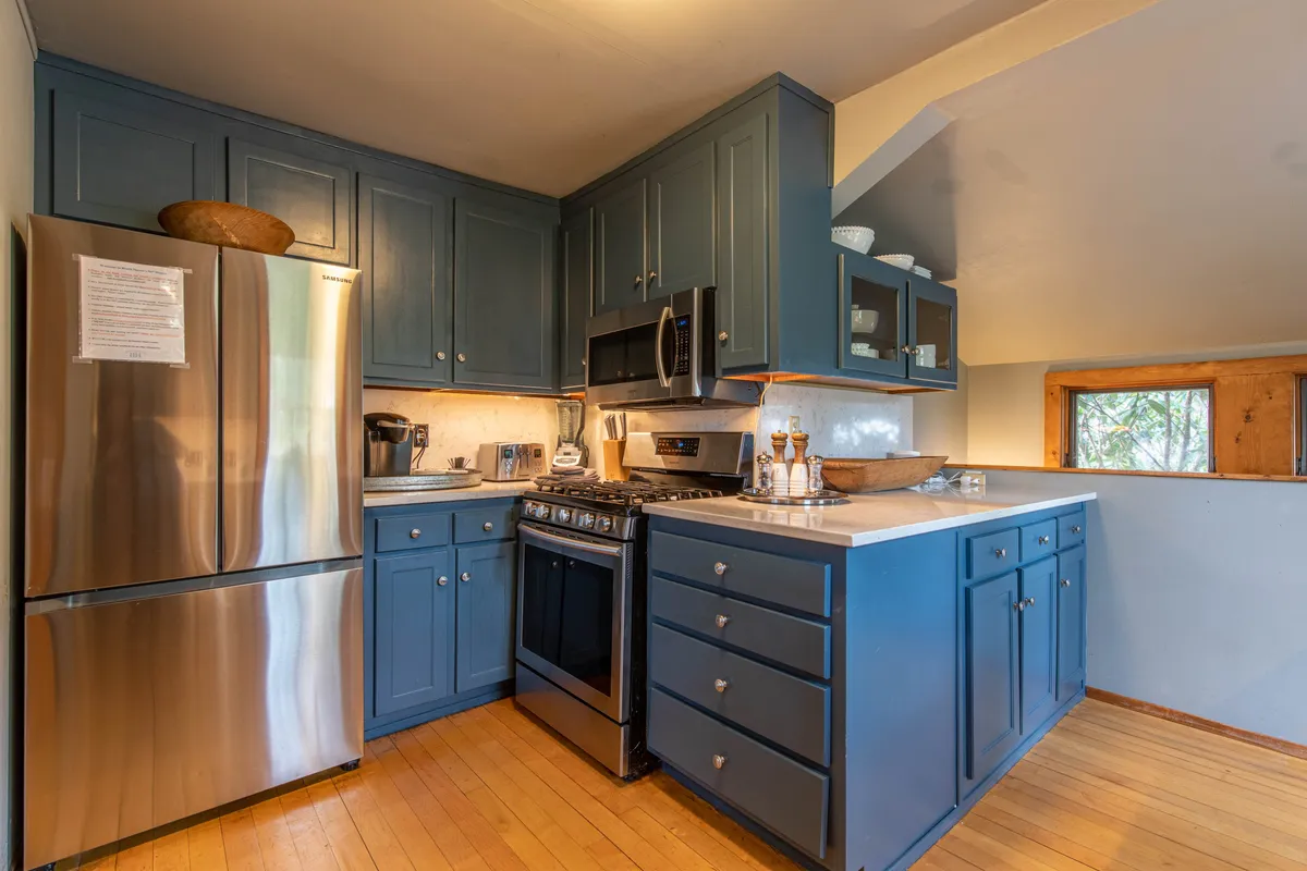 This image presents a close-up view of the kitchen’s stainless steel refrigerator, blue cabinetry, a gas stove, and a wooden countertop. It emphasizes the kitchen’s functionality and modern amenities, inviting guests to imagine cooking and gathering here.