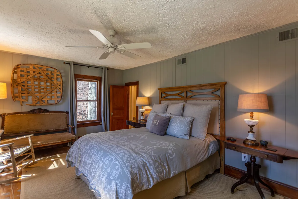 A serene bedroom featuring a bed with decorative pillows, wooden furniture, and a window letting in gentle natural light. The space feels calm, organized, and inviting, with a subtle blend of softness and rustic charm.