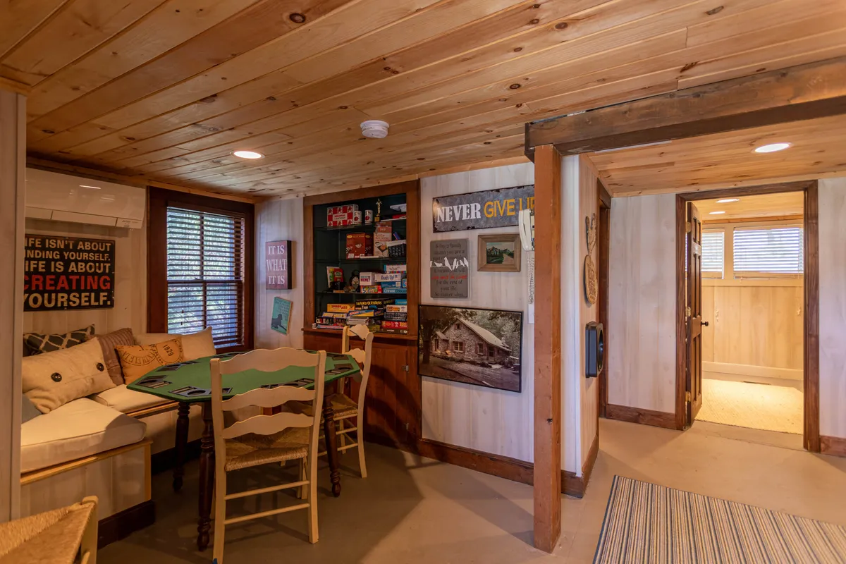 A warm, friendly sitting area featuring a game table surrounded by comfortable chairs, decorative wall art, and a bookshelf stocked with board games. The setup encourages social interaction, game nights, and shared laughter.