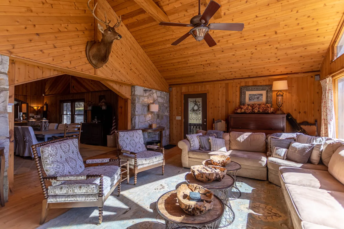 A cozy interior with a wooden ceiling, deer mount, comfortable seating arranged for conversation, and an ornate coffee table. The room exudes warmth and welcomes both group activities and quiet relaxation.