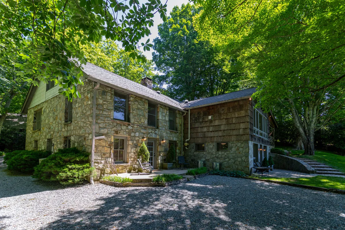 This exterior image features the stone façade of Beech Haven, surrounded by lush greenery and a gravel pathway. The scene is tranquil, evoking a sense of welcome and connection to nature. The open yard offers ample space for outdoor activities, and the inviting atmosphere is ideal for both people and pets.