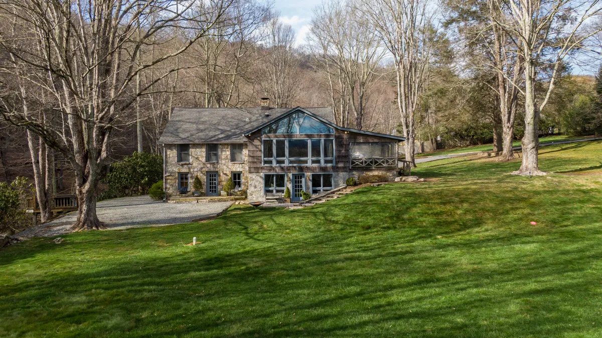 The stone exterior of the house is shown with large windows looking out onto an expansive lawn and mature trees. The spacious yard and natural setting invite outdoor gatherings and relaxation, echoing the exploration of local parks and lakes.