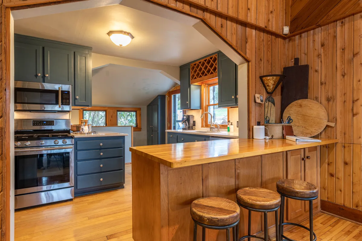 This image showcases a warm, inviting kitchen with a central island, bar stools, stainless steel appliances, and wood paneling. The island serves as the heart of the kitchen, perfect for meal prep and casual gatherings. The overall ambiance is cozy, blending rustic touches with modern convenience.