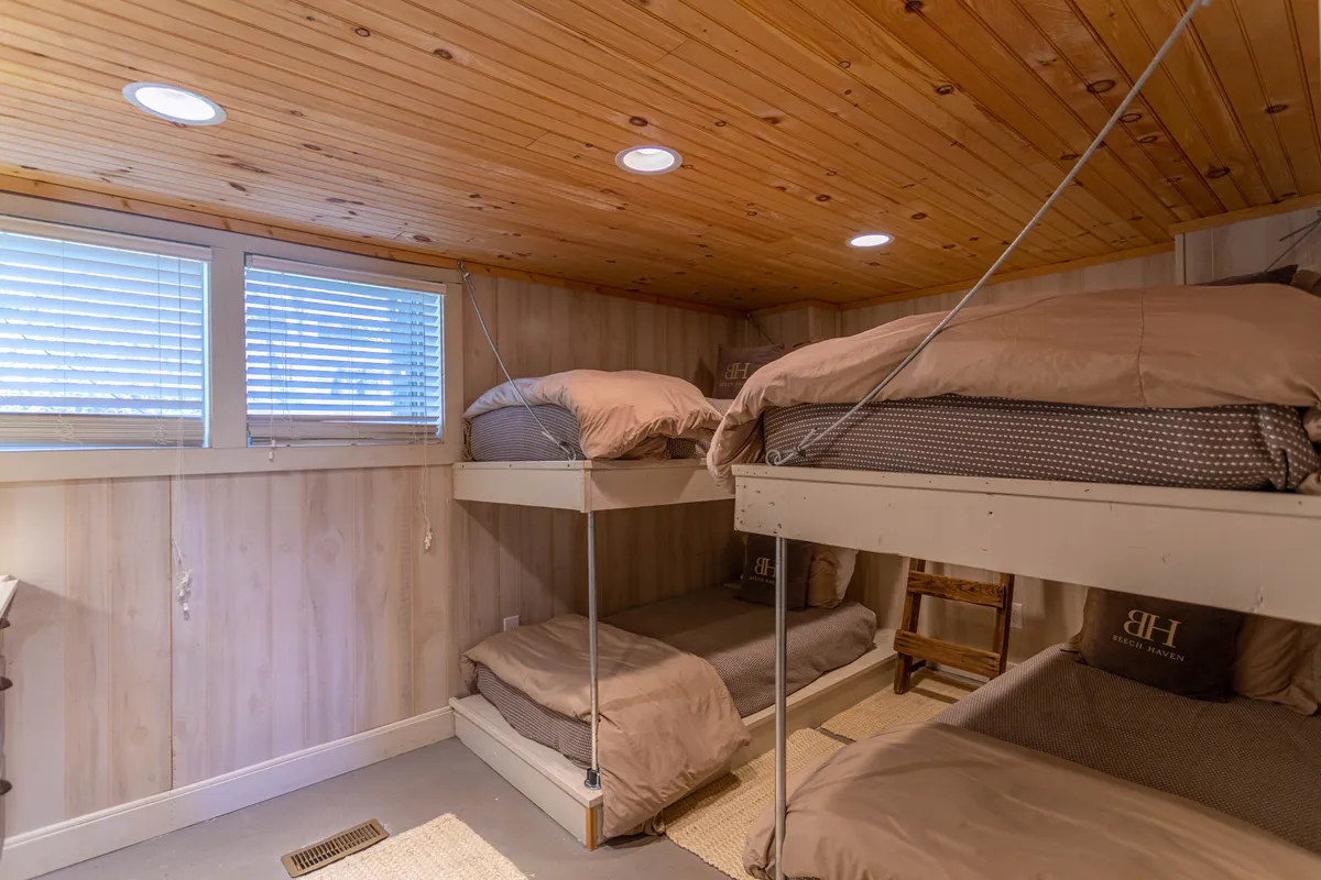 A cozy bunk room with wooden accents, featuring bunk beds made up with soft bedding and a textured wooden ceiling. The room feels playful yet comfortable, suitable for guests of all ages.